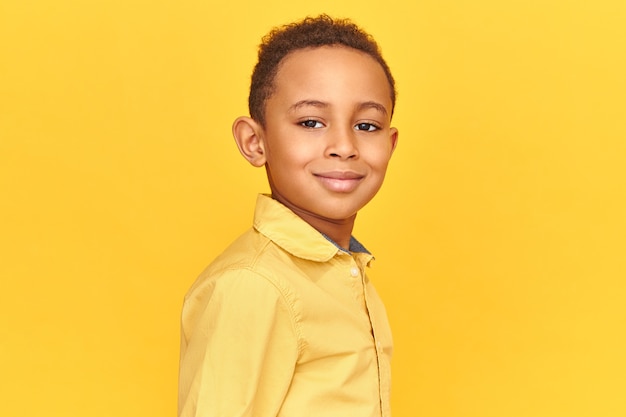 Free photo close up shot of handsome friendly looking boy in yellow shirt smiling, being in good mood posing isolated against blank background with copy space