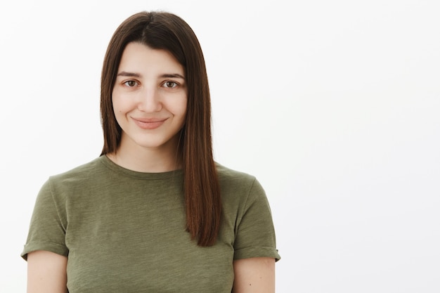 Free photo close-up shot of happy charming and tender cute young 20s brunette in olive t-shirt smiling shy and energized feeling optimistic gazing trustworthy over white wall