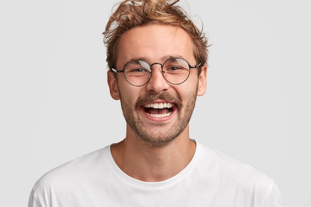 Close up shot of happy stylish man in round glasses, has positive smile on face, glad to recieve salary, going to spend money on new purchases