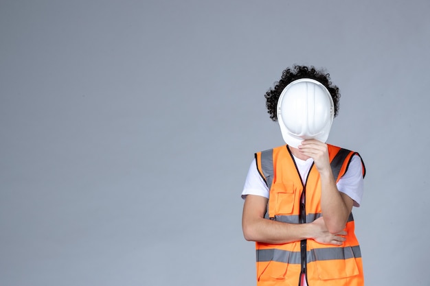 Free photo close up shot of nervous male constructor in warning vest taking off safety helmet over gray wave wall