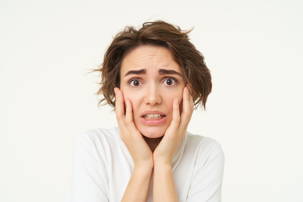 Close up shot of scared woman in panic touches her face and shaking from fear posing over white