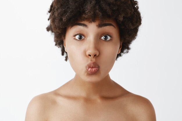 Close-up shot of tender and gentle naked woman with afro hairstyle folding lips and awaiting for passionate kiss or mwah