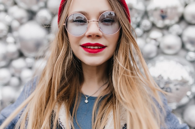 Free photo close-up shot of white pleased girl in glasses expressing interest. cheerful lady with red lips posing on sparkle wall.