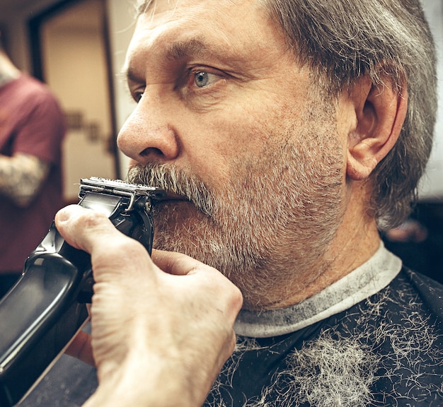 Free Photo close-up side view portrait of handsome senior bearded caucasian man getting beard grooming in modern barbershop.