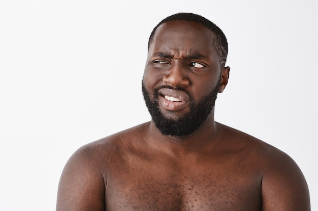 Close-up of skeptical and displeased young guy posing against the white wall