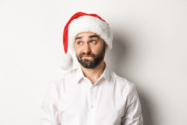 Close-up of skeptical guy in santa hat looking doubtful left, grimacing with hesitation 