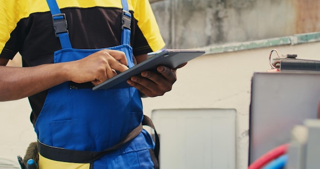 Free photo close up of skillful technician commissioned for outside hvac system routine maintenance, looking for refrigerant issues. meticulous mechanic doing air conditioner inspection, writing data on tablet