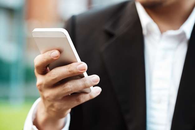 Free photo close-up smart business man wearing modern black suit and white shirt and texting on mobile smart phone