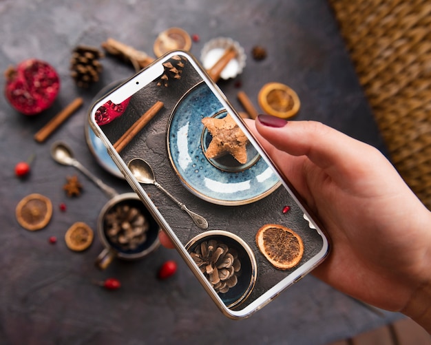 Close-up of smartphone held on top of cookie with dried citrus and pine cones