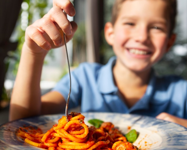 Free photo close up smiley boy eating spaghetti