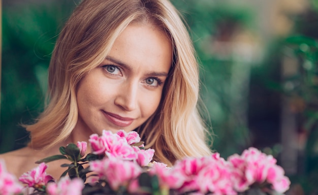 Close-up of smiling blonde young woman with pink flowers looking at camera