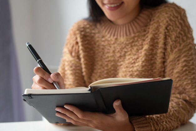 Close-up of smiling lady making notes about ideas in diary