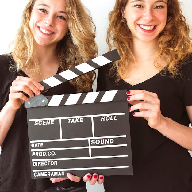 Close-up of smiling wins sister holding clapperboard in hands