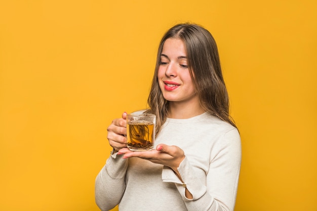 Close-up of smiling young woman looking at herbal tea in the glass cup