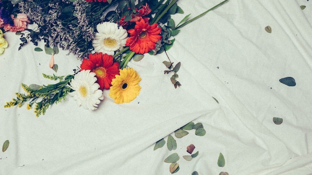 Close-up of solidago gigantea and colorful gerbera flowers on white cloth