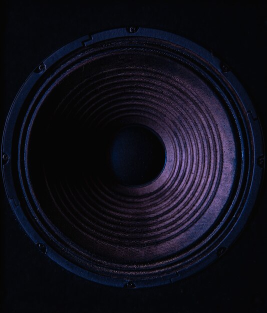 Close-up of speaker membrane on black background with colored lighting.