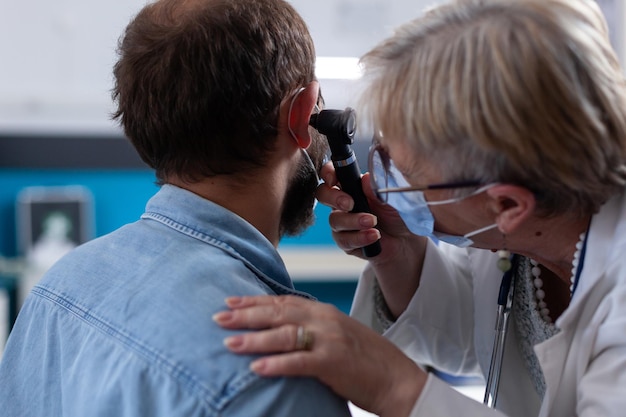 Free photo close up of specialist using otoscope to do ear examination with patient. woman otologist checking infection with otolaryngology instrument at medical visit during coronavirus pandemic.