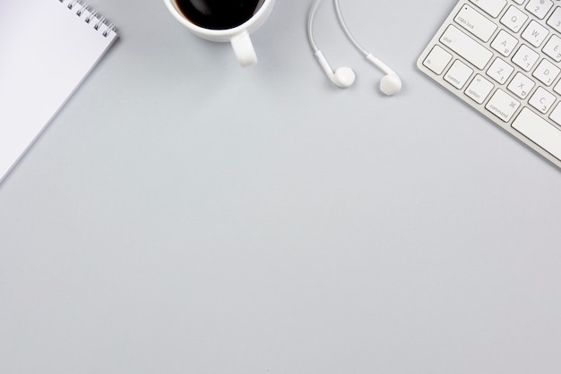 Free photo close-up of spiral notepad; coffee cup; earphone and keyboard on gray background