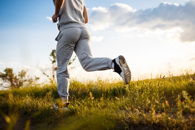 Close up of sportive man jogging in field at sunrise.