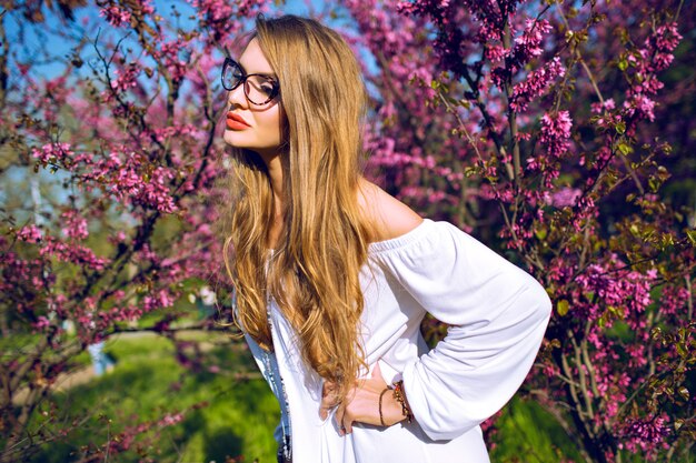 Close up spring summer portrait of stunning young woman with natural amazing long hairs and beauty face, wearing clear glasses, sunny colors.