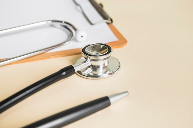 Close-up of stethoscope and clipboard with white paper on beige background