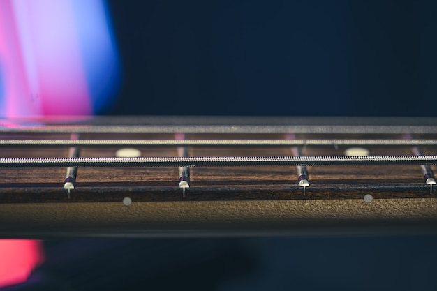 Close-up of strings on the fretboard of a bass guitar on a blurred dark background.