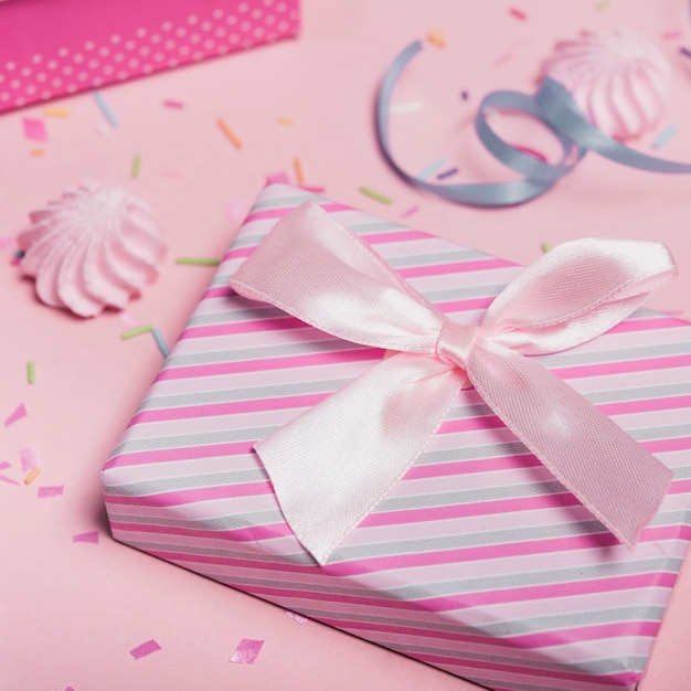 Close-up of striped gift box with satin bow against pink background