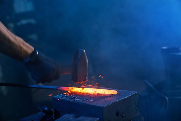 Free photo close up of strong male hands forging molten metal on anvil