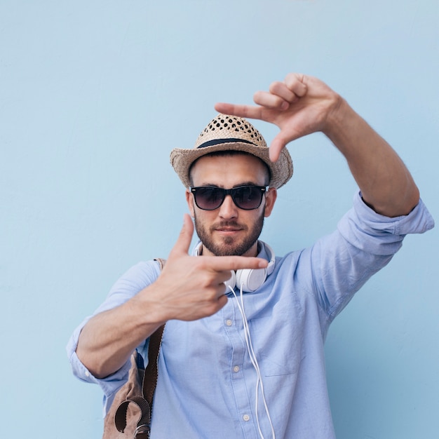 Free photo close-up of stylish young man making hand frame against blue wall