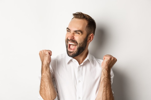 Close-up of successful caucasian man rejoicing, making fist pump and shouting of joy, looking left, winning, standing  