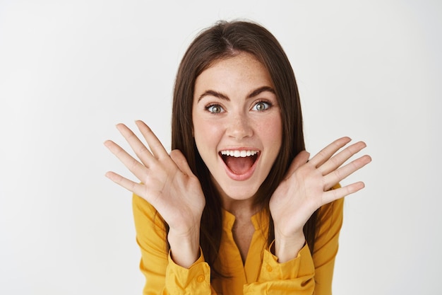 Free photo close-up of surprised and excited woman reacting on sale promo, looking at front happy and amazed, standing over white wall