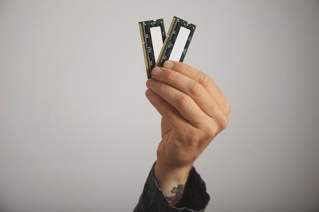 Close up of a tattooed man's hand with two RAM planks with chips on white wall