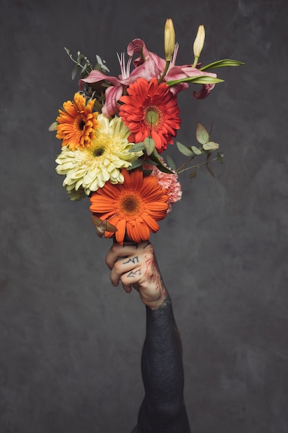 Free photo close-up of tattooed young man holding floral bouquet in hand against grey wall