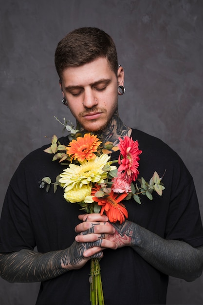 Close-up of a tattooed young man holding flowers in hand praying