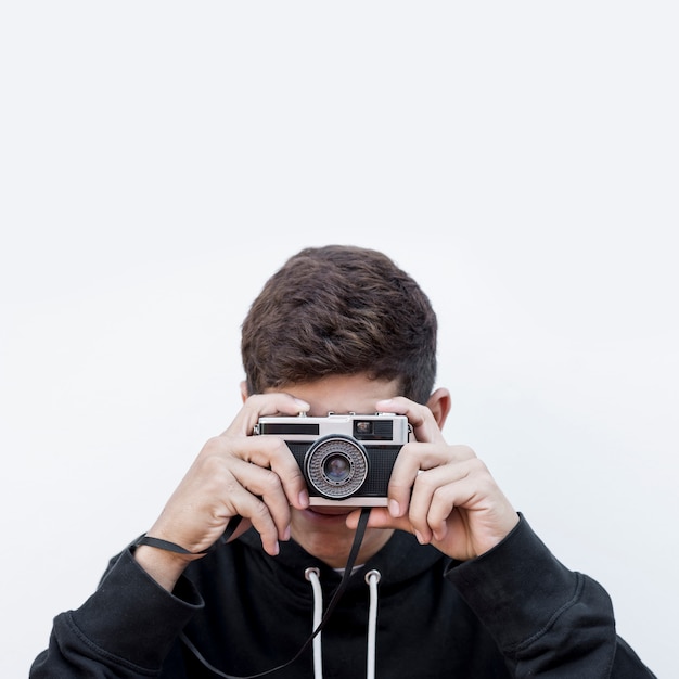 Close-up of a teenage boy taking photography click on retro vintage photo camera against white background