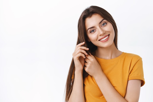 Close-up tender, feminine alluring girlfriend taking care of her hair, touching strands tilt head and smiling, satisfied with good haircare product she applied to make hairstyle, white background