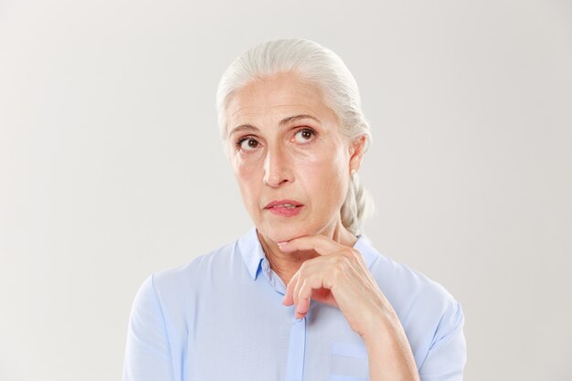 Close-up of thinking beautiful old woman in blue shirt, looking up