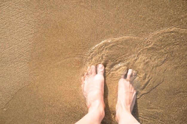 Close-up top view of feet in wet sand