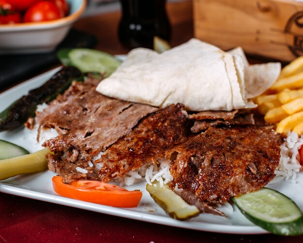 Close up of turkish kebab meat with rice french fries and fresh vegetables on a plate