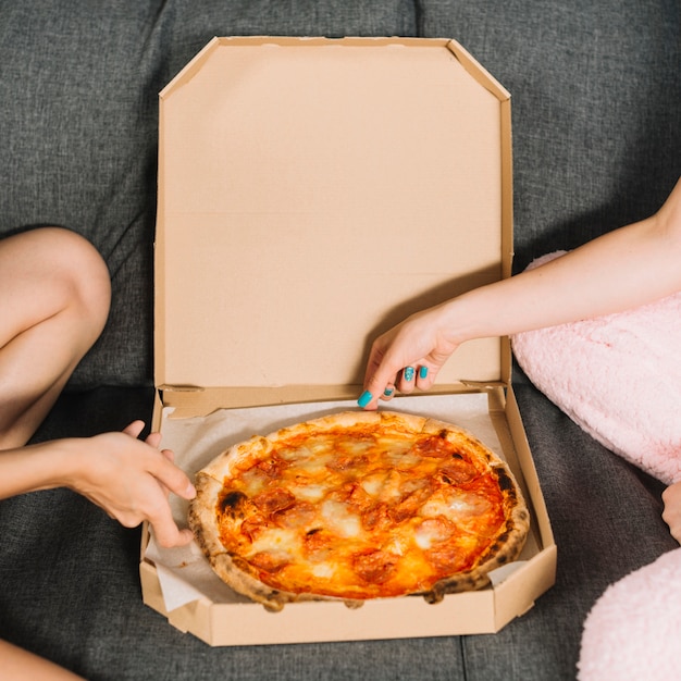 Close-up of two female friends taking pizza slices from box