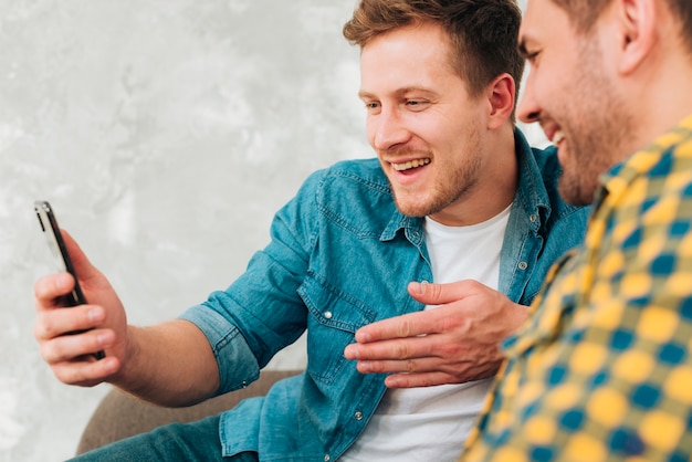 Close-up of two male friends sitting together watching on mobile phone