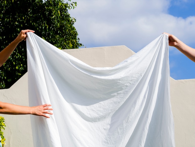 Free Photo close up two people hanging a white sheet on the line