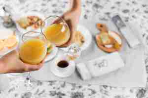 Free photo close-up of a two people toasting juice glasses over the breakfast on table