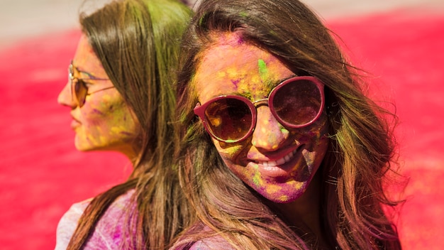 Free photo close-up of two women wearing sunglasses covered with holi color powder