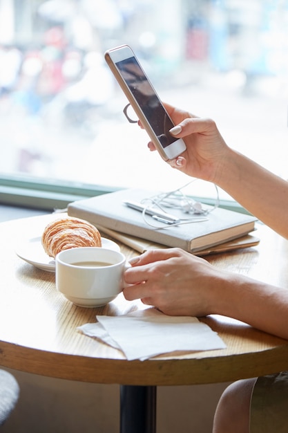 Close up of unrecognizable female hands holding the phone and cup of coffee