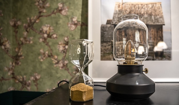 Free photo close-up of an unusual shaped glass hourglass and a vintage lamp on a blurred background.