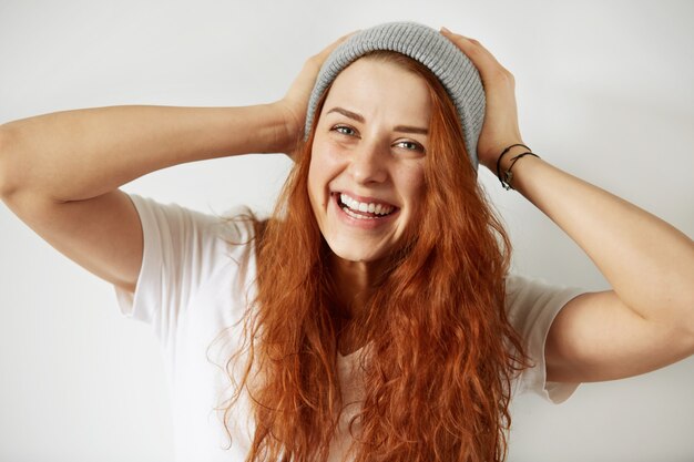 Close up view of attractive young girl with long loose red hair, wearing white T-shirt and gray cap