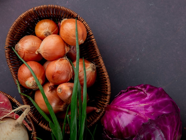 Close-up view of basket full of onion with purple cabbage and scallion on maroon background with copy space