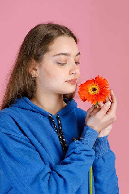 Free photo close up view of beautiful girl admiring delicate orange gerbera flower while inhaling aroma