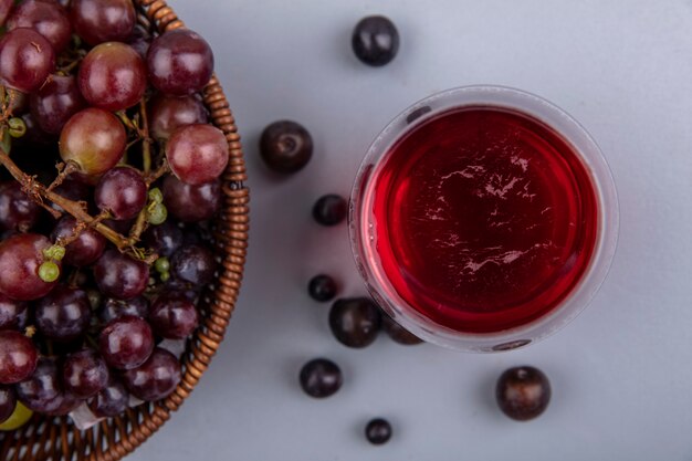 Close-up view of black grape juice in glass with grapes in basket and on gray background